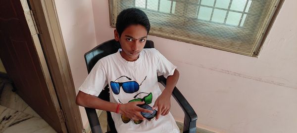 Portrait of young man standing against window at home