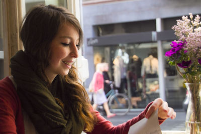 Smiling young woman reading menu while sitting by window in cafe