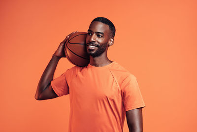 Man with basketball standing against orange background