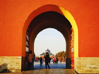 People walking on archway against orange sky