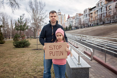 Middle aged father with daughter holding a poster with anti-war message over cityscape background