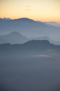 Scenic view of mountains in foggy weather during sunrise