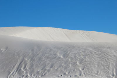 Low angle view of sand dune against clear blue sky