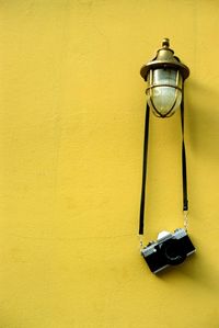 Low angle view of electric lamp hanging on yellow wall