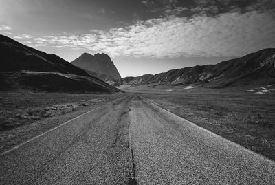 Empty road on landscape by mountains against sky