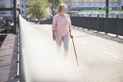 Senior woman walking on footbridge, using walking stick