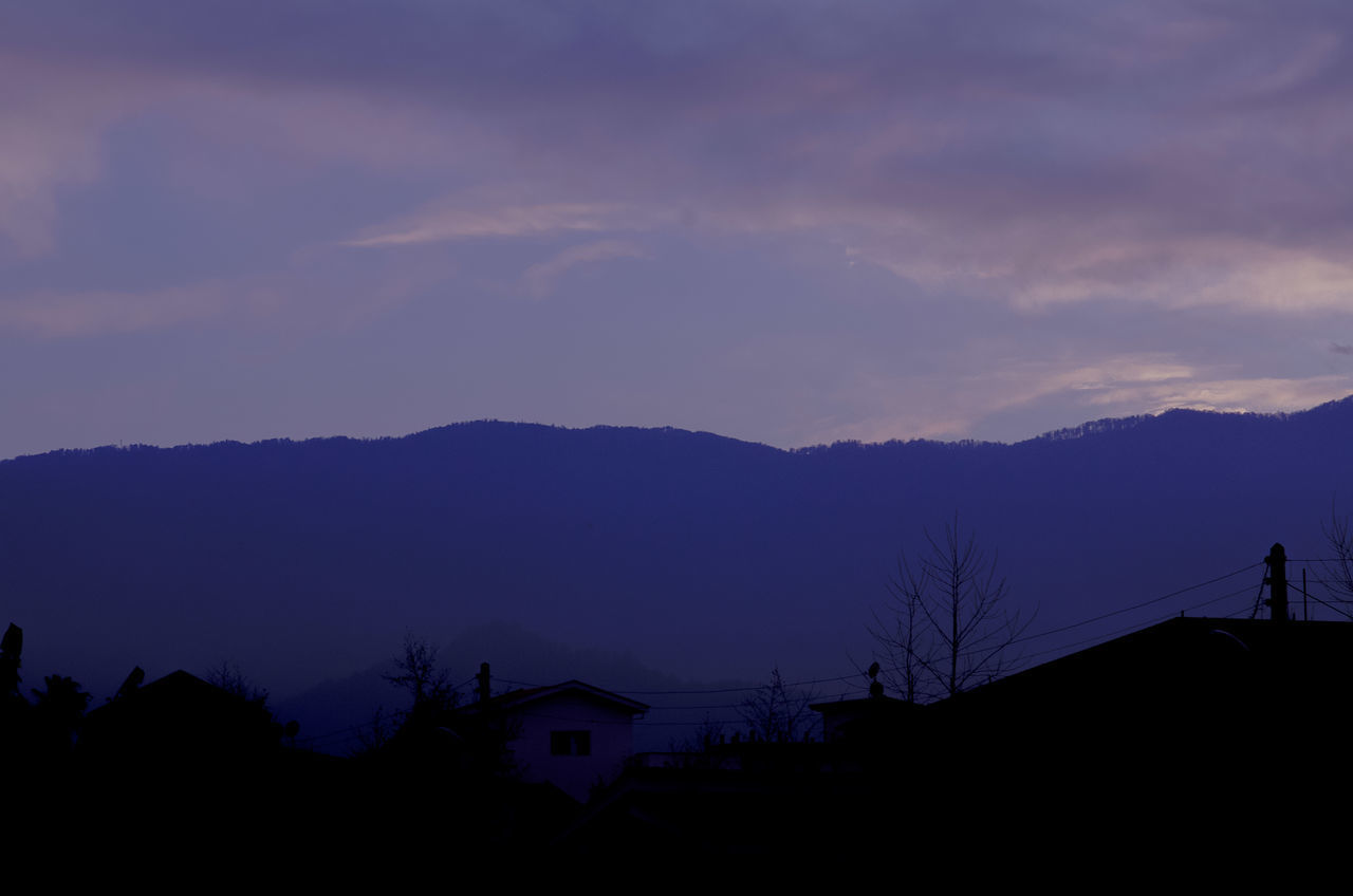 SILHOUETTE HOUSES AND MOUNTAINS AGAINST SKY DURING SUNSET