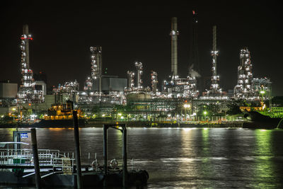 Illuminated factory by river against sky at night