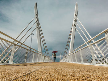 Rear view of woman walking on bridge against cloudy sky