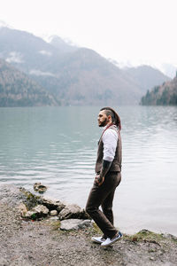 A serious lonely brutal hipster man in a wedding suit by the sea and mountains in nature outdoors