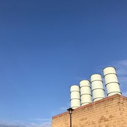 Low angle view of smoke stacks against clear blue sky