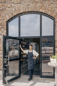 Portrait of female owner standing with hand on hip at cafe doorway