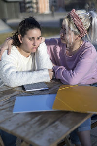 Woman consoling sad friend at table in yard