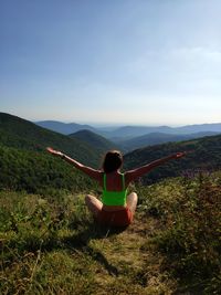 Rear view of woman with arms outstretched sitting on mountain