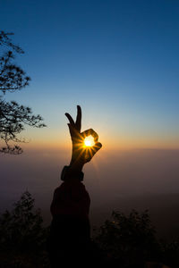 Silhouette hand of woman showing ok sign against clear sky during sunset