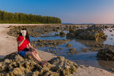 Woman covering face with equipment while sitting at beach