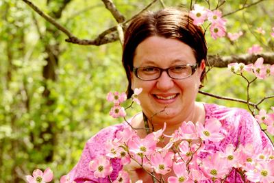 Portrait of smiling woman standing by pink flowers growing outdoors