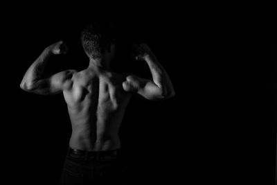 Rear view of shirtless man against black background