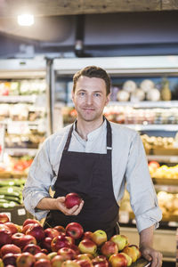 Portrait of confident smiling entrepreneur holding apple while standing in supermarket