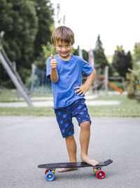 Full length portrait of boy with skateboard showing thumbs up sign on road