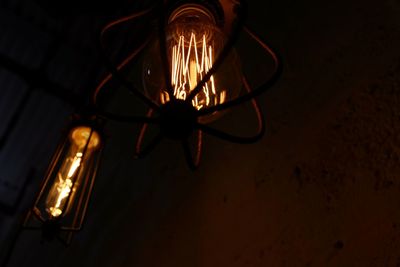 Low angle view of illuminated light bulb hanging on ceiling