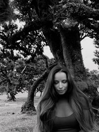 Portrait of young woman standing against tree trunk