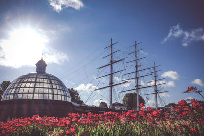 Low angle view of flowering plants and tall ship against cloudy sky