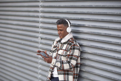 Portrait of a happy man listening to music on headphones while texting on his phone
