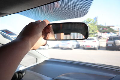 Cropped hand of person adjusting rear-view mirror in car