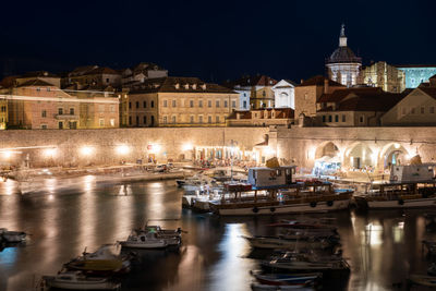 Boats moored in river against buildings at night