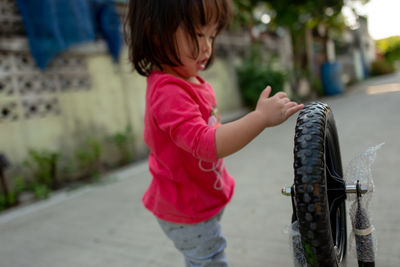 Close-up of cute girl playing with bicycle wheel outdoors