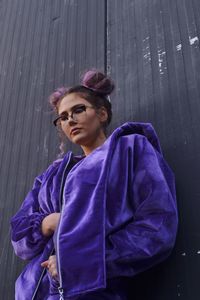 Low angle view of young woman wearing purple jacket by wall