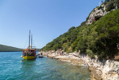 Boat moored in sea by rock formation against clear blue sky