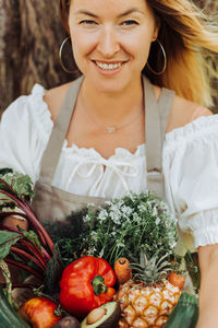 Close up of young woman holding basket of vegetables and smiling