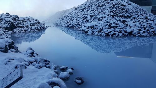 Snow covered rocks by lake against sky