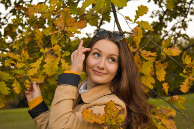 Smiling young woman amidst tree branches during autumn