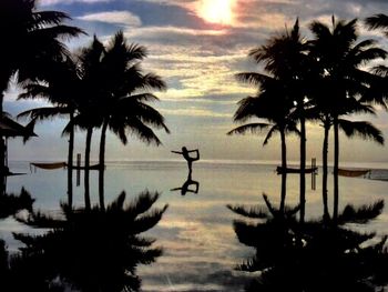 Silhouette palm trees by lake against sky at sunset