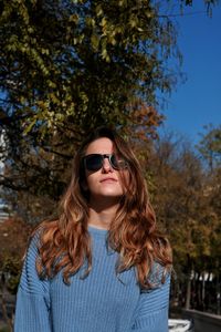 Portrait of young woman wearing sunglasses standing against trees