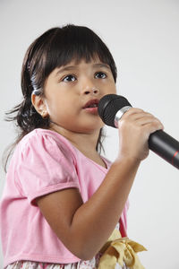 Close-up of girl singing through microphone against white background