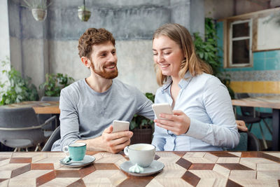 Cheerful couple using mobile phone at cafe