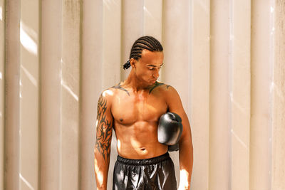 Shirtless man with boxing glove standing against wall