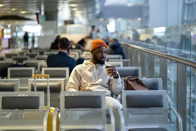 Young african man drinking coffee and eating sandwich while waiting for flying at airport terminal