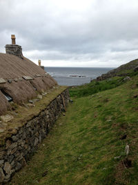 Hut on hill by sea against cloudy sky