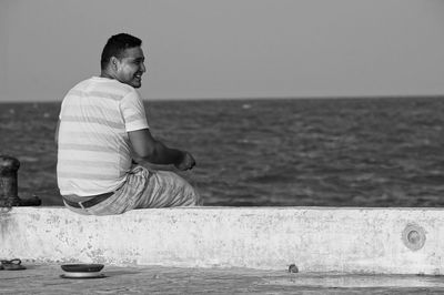 Side view of man sitting on beach against clear sky