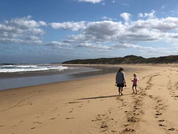 Mother and daughter walking at beach against sky