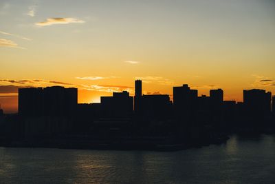 Silhouette buildings by river against sky during sunset