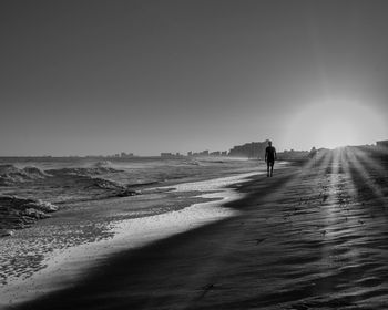 Man walking on shore by sea against sky during sunset