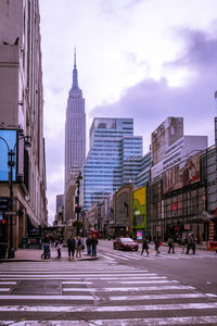 People walking on road by buildings against sky