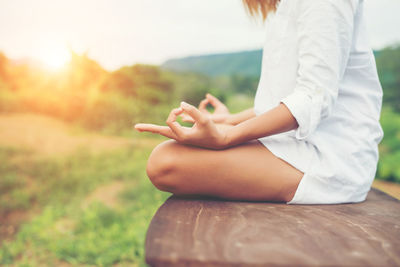 Midsection of woman doing yoga on tree stump at field