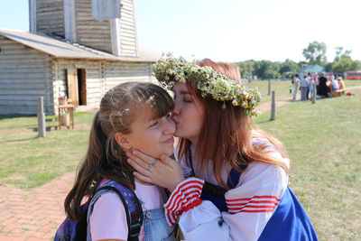 Woman in traditional clothing kissing girl while standing outdoors